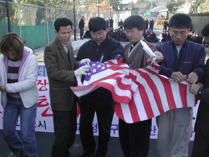 집회에 참석한 신부와 사회단체 대표들이 미 고문단 정문 앞에서 항의의 뜻으로 성조기를 찢고 있다. 